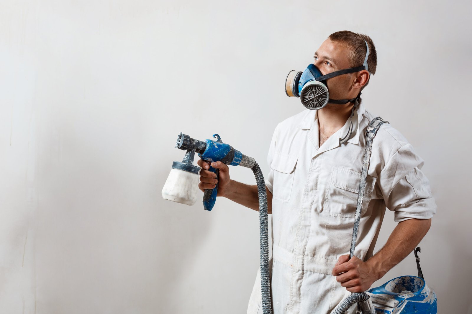 worker painting wall with spray gun in white color.